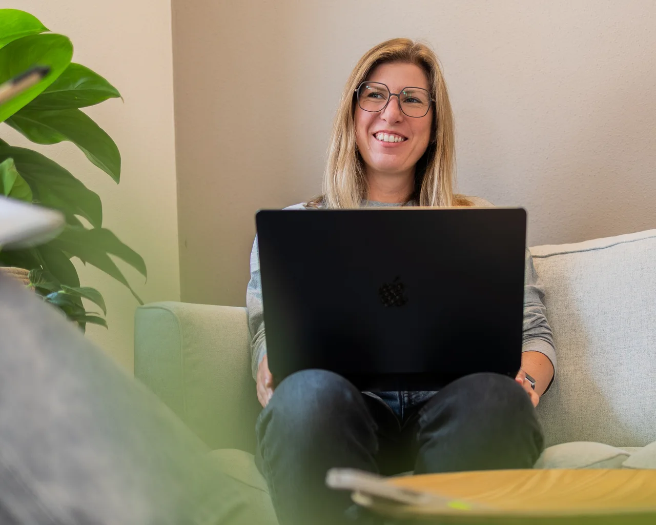 Stefanie Seitz sitzt mit einem Laptop auf dem Sofa und lächelt in die Kamera.